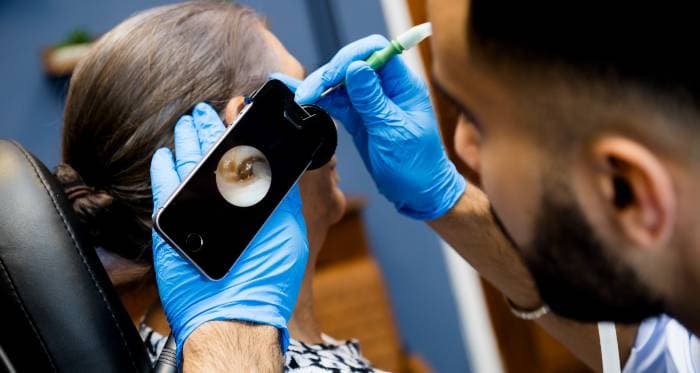 Audiologist examining a patient's ear using a smartphone camera for magnification.