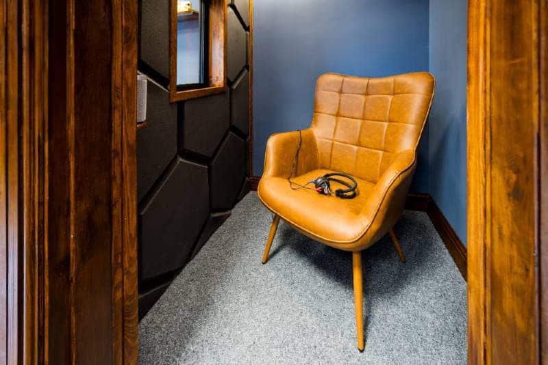 A caramel-coloured leather chair in a corner of a blue-walled room with wooden door frames, and headphones resting on the seat.