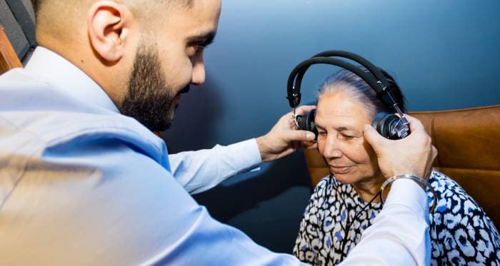 A young man assists an elderly woman in putting on headphones.