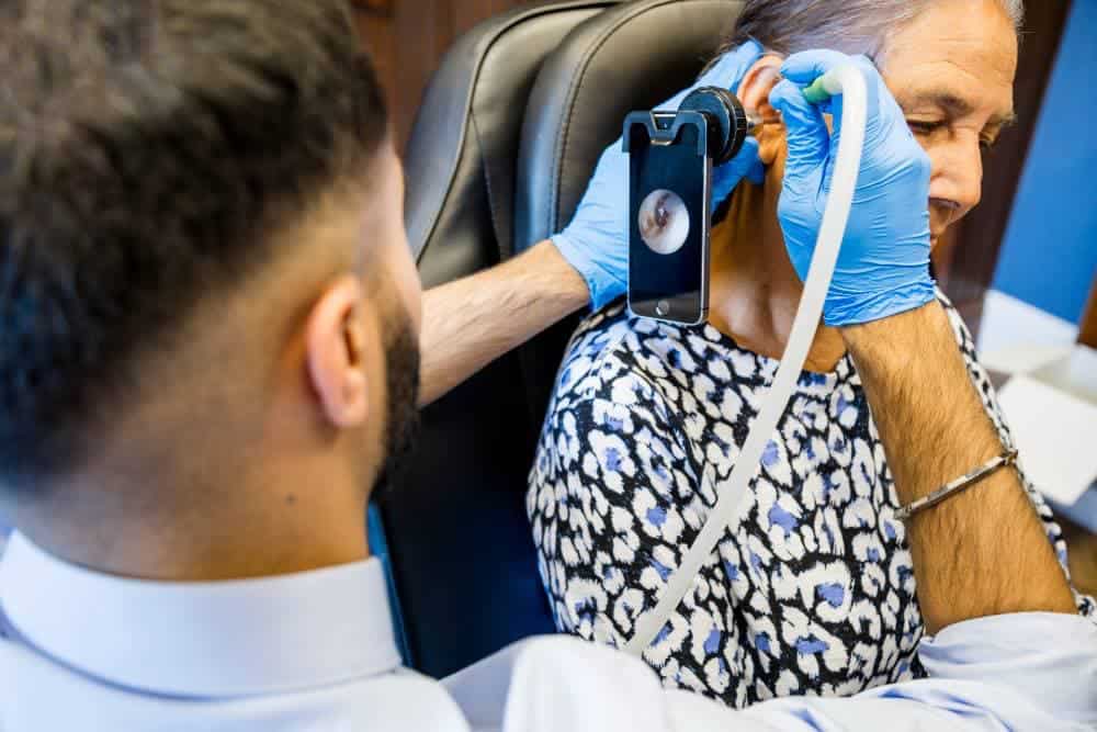 A doctor using a smartphone attached to a device to examine an elderly woman's ear in a medical office.