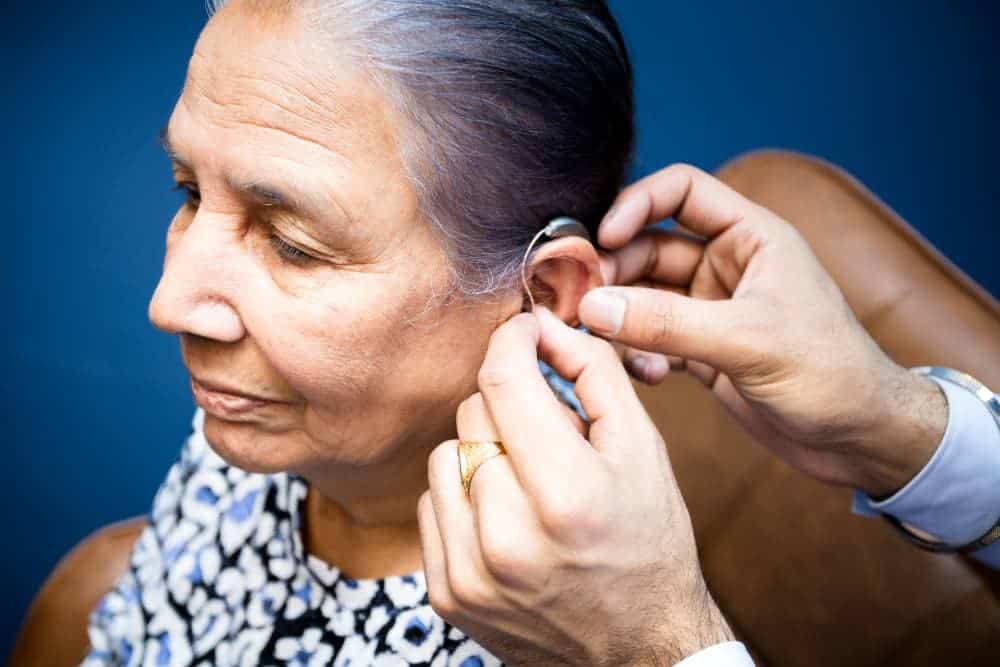 A healthcare professional is assisting an elderly woman by fitting a hearing aid into her ear.